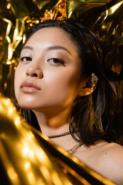 Portrait of beautiful asian young woman with wet short hair posing next to shiny golden background, model, looking at camera, wrinkled yellow foil, natural asian beauty — Stock Photo