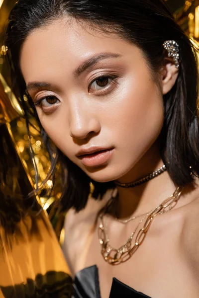 Primo piano di seducente asiatica giovane donna con i capelli corti bagnati posa accanto a sfondo giallo lucido, modello, guardando la fotocamera, rugosa lamina d'oro, trucco naturale, bellezza — Foto stock