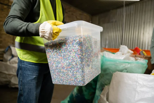 Ausgeschnittene Ansicht des Arbeiters in Warnweste und Handschuhaufbewahrungsbehälter mit Kunststoff zum Recyceln während der Arbeit im Müllsortierzentrum, Müllsortier- und Recyclingkonzept — Stockfoto