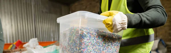 Cropped view of sorter in protective vest and glove holding container with plastic for recycle while working in blurred garbage sorting center, garbage sorting and recycling concept, banner — Stock Photo