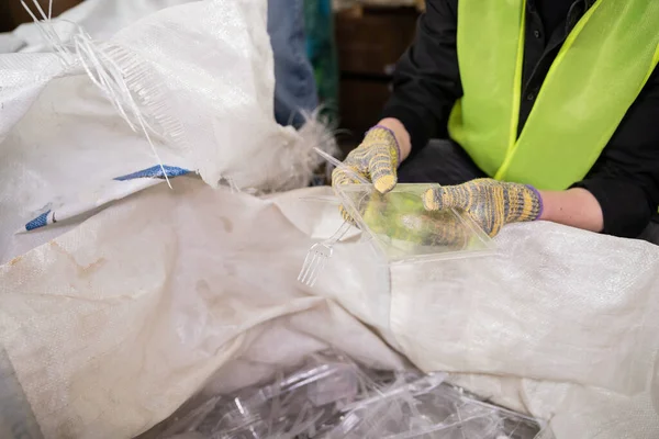 Ausgeschnittene Ansicht eines Arbeiters in Schutzhandschuhen und Sicherheitsweste, der Plastikmüll in der Nähe von Sack zum Recyceln hält, während er in einer Müllentsorgungsstation arbeitet, Müllsortier- und Recyclingkonzept — Stockfoto