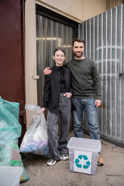 Lächelnde Ehrenamtliche, die im Stehen in die Kamera schauen, reißen Müll und Tür der Entsorgungsstation im Freien auf, Mülltrennung und Recyclingkonzept — Stockfoto