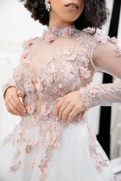 Ausgeschnittene Ansicht einer brünetten Frau, die in einem wunderschönen und floralen Hochzeitskleid in einem luxuriösen Salon um weiße Tüll-Stoffe steht, Brautshopping, zukünftige Braut, Details — Stockfoto