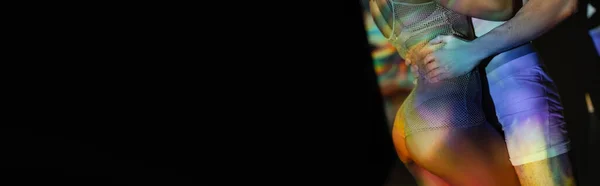 Vista parcial del hombre en calzoncillos abrazando a la mujer afroamericana con nalgas sexy, en un elegante traje de red en el fondo con efectos de iluminación de colores y espacio de copia negro, pancarta - foto de stock