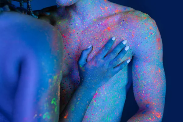 Partial view of young and passionate african american woman touching bare-chested man with muscular body while standing on blue background with cyan lighting — Stock Photo