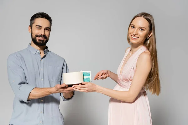 Cheerful and stylish couple looking at camera while cutting blue cake during baby shower celebration on grey background, expecting parents concept, gender party, it`s a boy — Stock Photo
