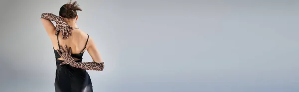 Modisches Frühjahrskonzept, Rückansicht einer jungen Frau mit brünetten Haaren in ausdrucksstarker Pose im schwarzen Trägerkleid und Handschuhen mit Animal Print auf grauem Hintergrund, Banner — Stockfoto