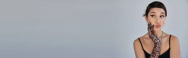 Primavera fotografia di moda, ritratto di donna asiatica premurosa con capelli castani e trucco audace guardando lontano su sfondo grigio, abito cinturino nero, guanto di stampa animale, banner — Foto stock