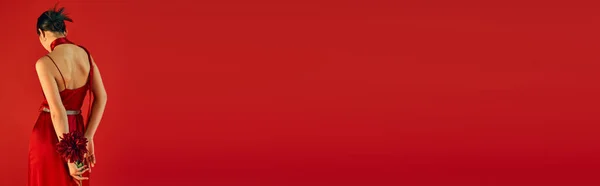 Vista posterior de la mujer elegante y juvenil con el pelo moreno celebración de peonía de color burdeos mientras que de pie en vestido de moda sobre fondo rojo con espacio para copiar, concepto de primavera de moda, bandera — Stock Photo