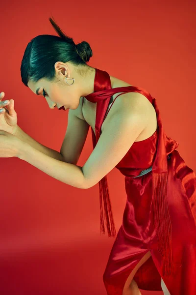 Стильная азиатская модель с модной прической и смелым макияжем позирует в элегантном платье и шейном платке на красном фоне, модный весенний, очаровательный, гламурный, изящный, поколение z — стоковое фото