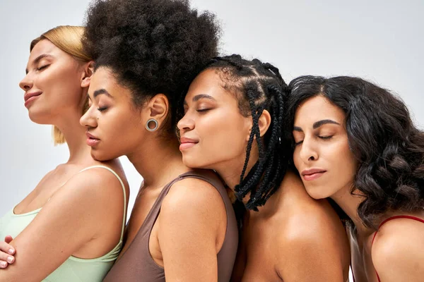 Multiethnische Frauen in bunten BHs stehen nebeneinander und schließen die Augen, während sie isoliert auf grauen, unterschiedlichen Körpertypen und Selbstakzeptanzkonzepten posieren, multikulturelle Modelle — Stockfoto