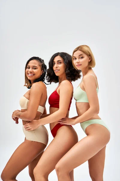 Cheerful young african american woman in stylish lingerie looking at camera and posing near multiethnic models isolated on grey, different body types and self-acceptance concept, multicultural models — Stock Photo