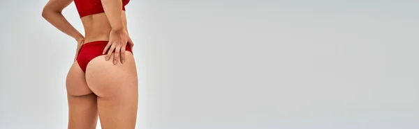 Vista ritagliata di donna sexy in mutandine rosse moderne e reggiseno toccare fianchi e posa isolata su grigio con spazio copia, auto-accettazione e concetto positivo per il corpo, banner — Foto stock