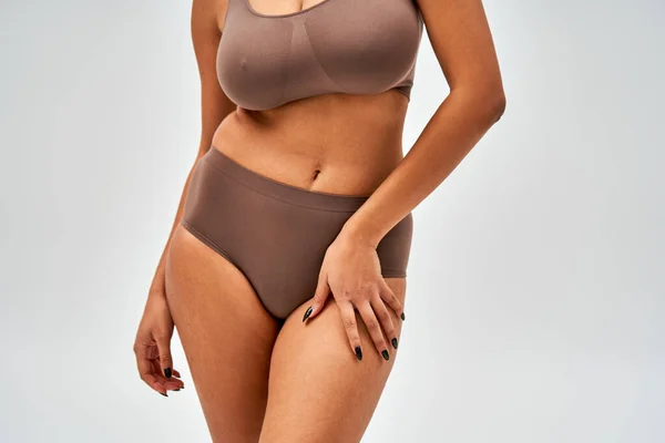 Cropped view of african american woman in modern brown panties and bra touching hip and standing isolated on grey, self-acceptance and body positive concept — Stock Photo