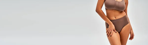 Vista cortada da mulher americana africana sexy em sutiã marrom e calcinha tocando quadril enquanto estava isolado em cinza, auto-aceitação e corpo conceito positivo, banner com espaço de cópia — Fotografia de Stock