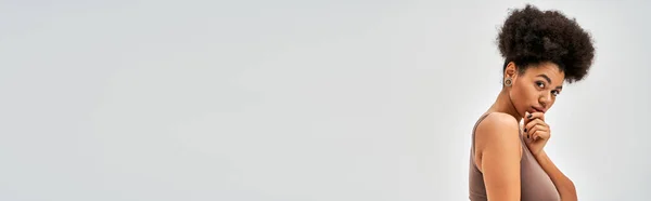 Ritratto di donna africana americana fiduciosa in lingerie marrone che tocca il mento e guarda la macchina fotografica mentre si trova isolata sul concetto di grigio, accettazione di sé e positivo per il corpo, banner — Foto stock