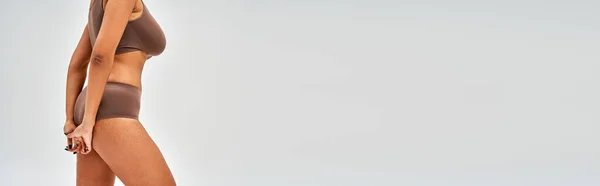 Ausgeschnittene Ansicht einer verführerischen afrikanisch-amerikanischen Frau in modernen braunen Dessous, die isoliert auf Grau steht, Selbstakzeptanz und ein körperpositives Konzept, Banner mit Kopierraum — Stockfoto