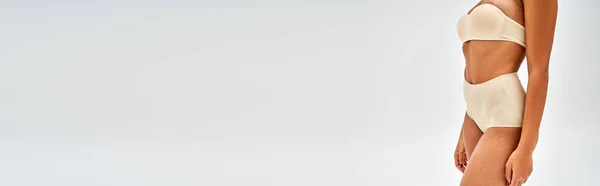 Vista recortada do jovem modelo afro-americano em lingerie bege moderna em pé isolado em cinza, auto-aceitação e corpo conceito positivo, banner com espaço de cópia — Fotografia de Stock