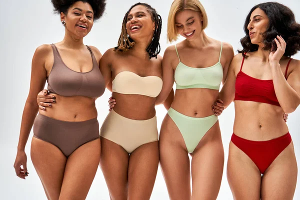 Confident and sexy multiethnic women in colorful lingerie hugging each other while posing and standing isolated on grey, different body types and self-acceptance, multicultural representation — Stock Photo