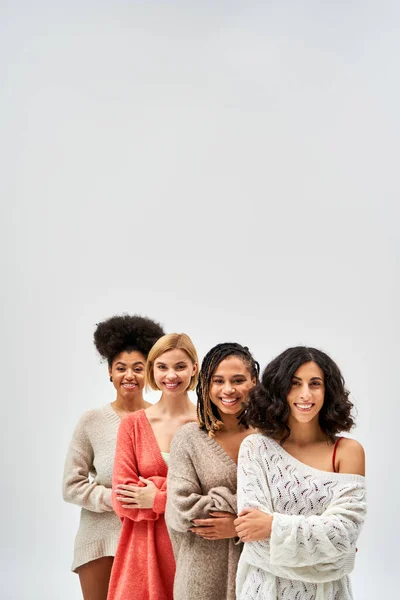 Positive multiethnische Frauen in stylischen Strickpullovern, die die Arme verschränken und in die Kamera schauen, während sie isoliert auf grauen, unterschiedlichen Körpertypen und Selbstakzeptanz stehen, multikulturelle Repräsentation — Stockfoto