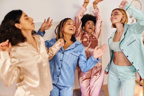 Aufgeregt und fröhlich multiethnische Freundinnen in bunten Pyjama tanzen und gemeinsam Spaß haben bei Pyjama-Party zu Hause, Bonding-Zeit in bequemer Nachtwäsche — Stockfoto