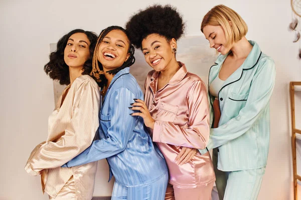 Glückliche multikulturelle Freundinnen im bunten Pyjama, die in die Kamera schauen, Spaß haben und sich bei Pyjama-Party zu Hause umarmen, Zeit in bequemer Nachtwäsche verbringen, kulturelle Vielfalt — Stock Photo