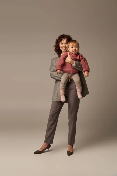 Якісний час, кар'єра та сім'я, щаслива жінка у костюмі, що тримає дитину на сірому фоні, зростання та сім'ю, любляче материнство, спосіб життя, багатозадачність, концепція гармонії трудового життя — стокове фото
