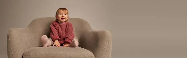 Niedliches Baby-Mädchen, Kleinkind in Freizeitkleidung auf bequemem Sessel auf grauem Hintergrund im Atelier sitzend, Emotion, Glück, Freude, Unschuld, kleines Kind, Kleinkindmode, stilvolles Outfit, Banner — Stockfoto