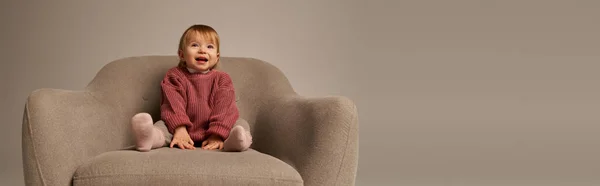 Carino bambina, bambino in abbigliamento casual seduto su comoda poltrona su sfondo grigio in studio, emozione, felicità, gioia, innocenza, bambino piccolo, moda bambino, vestito elegante, banner — Foto stock