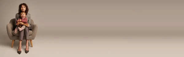 Equilibrio tra lavoro e concetto di vita, donna d'affari in giacca e cravatta seduta sulla poltrona con la figlia del bambino, giocando con biplano in legno, sfondo grigio, maternità, carriera e famiglia, striscione — Foto stock