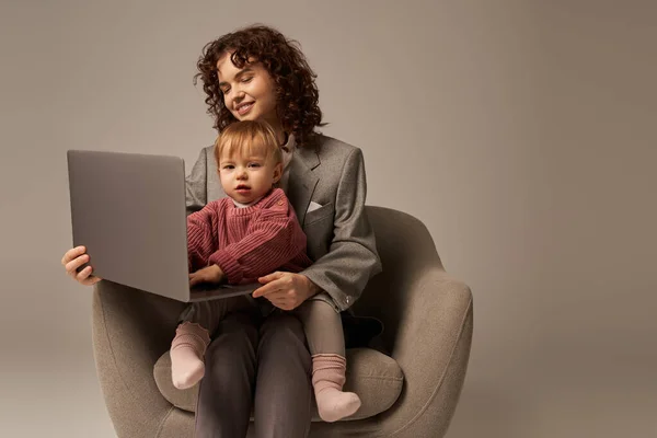 Building successful career, work life success, working parent, happy businesswoman using laptop and sitting on armchair with daughter, mother and child, motherhood, multitasking — Stock Photo