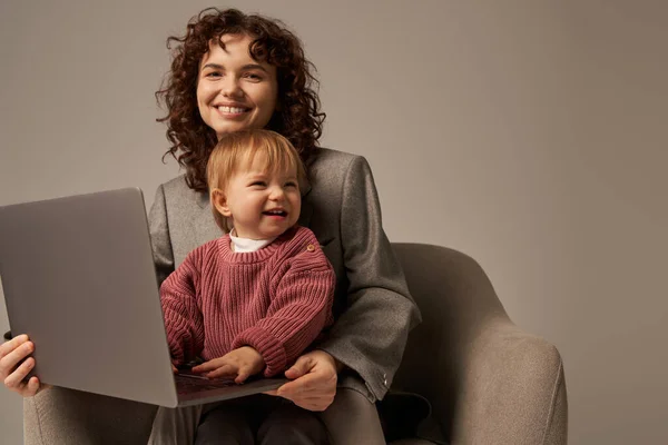 Building successful career, balanced lifestyle, working parent, happy businesswoman using laptop and sitting on armchair with daughter, mother and child, motherhood, multitasking, growth and family — Stock Photo