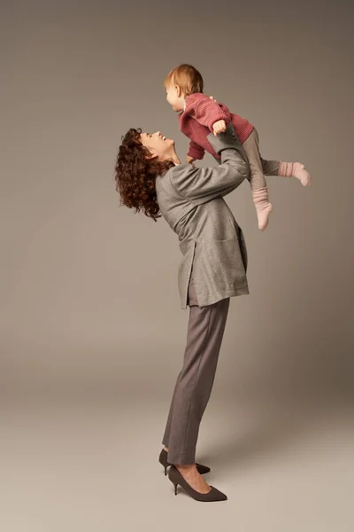 Tempo de qualidade, parentalidade e carreira, empresária alegre levantando sua filha criança em fundo cinza, conceito de harmonia de vida no trabalho, pai trabalhador, maternidade amorosa, comprimento total — Fotografia de Stock