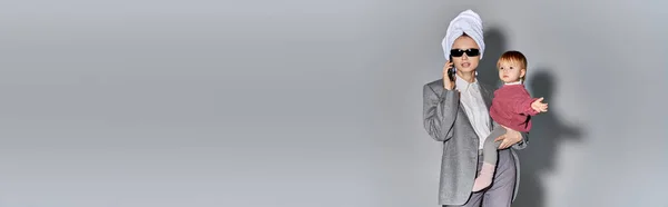 Carrière et famille, femme en lunettes de soleil tenant dans les bras fille tout-petit et debout avec serviette sur la tête, mode de vie équilibré, femme d'affaires parlant sur smartphone sur fond gris, bannière — Photo de stock
