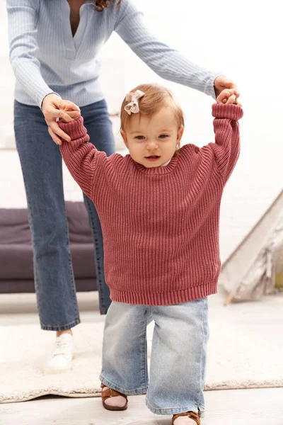 Збалансований спосіб життя, сімейні відносини, працююча мати тримає руки з дочкою малюка, перші кроки, якісний час, зв'язок, спокій, затишна вітальня, джинсові джинси, повсякденний одяг — стокове фото