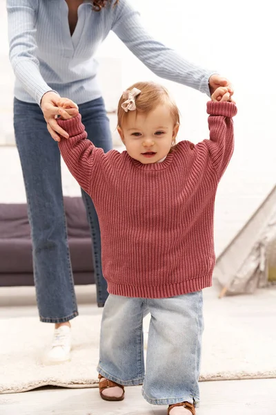Balanced lifestyle, family relationships, working mother holding hands with toddler daughter, first steps, quality time, bonding, togetherness, cozy living room, denim jeans, casual attire — Stock Photo