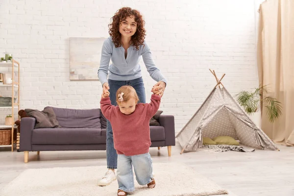 Primi passi, tempo di qualità, legame, equilibrio tra lavoro e vita, rapporti familiari, madre che lavora tenendosi per mano con la figlia del bambino, insieme, accogliente soggiorno, jeans denim, interno — Foto stock