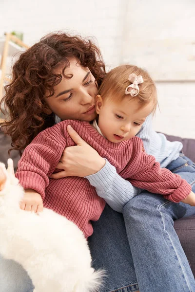 Engaging with kid, happy woman kissing toddler daughter in cozy living room, playing with rabbit, quality time, casual attire, bonding between mother and child, stuffed animal — Stock Photo