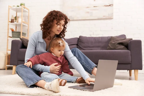 Modern working parent, engaging with child, balancing work and life, curly woman using laptop in cozy living room, modern parenting, multitasking woman, freelance, building successful career — Stock Photo