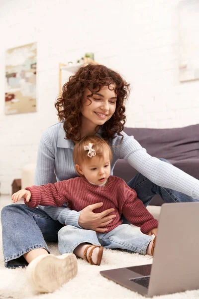 Moderno padre que trabaja, comprometiendo con el niño, equilibrando el trabajo y la vida, mujer feliz usando el ordenador portátil en la sala de estar acogedora, crianza moderna, mujer multitarea, independiente, la construcción de una carrera exitosa - foto de stock