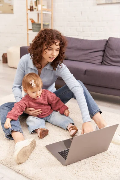 Multitasking woman, freelance, modern working parent, engaging with child, balancing work and life, curly woman using laptop in cozy living room, modern parenting, building successful career — Stock Photo