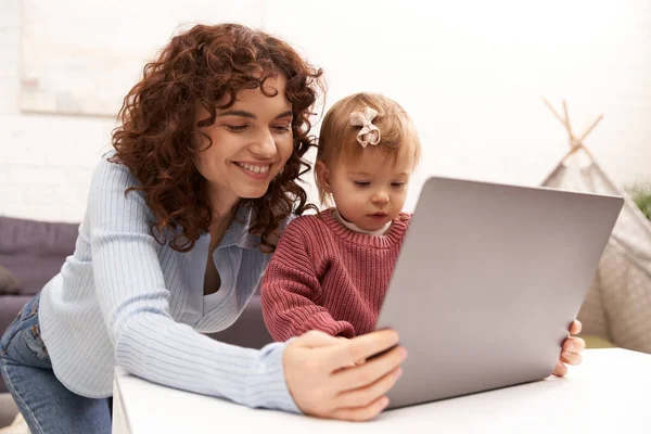 Multitasking woman, freelance, modern working parent, balancing work and life, happy woman using laptop in cozy living room, modern parenting, building successful career, engaging with child — Stock Photo