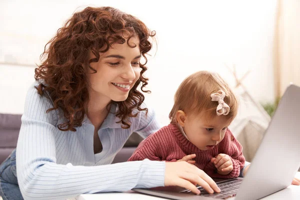 Multitasking woman, freelance, modern working parent, balancing work and life, cheerful woman using laptop in cozy living room, modern parenting, building successful career, engaging with child — Stock Photo