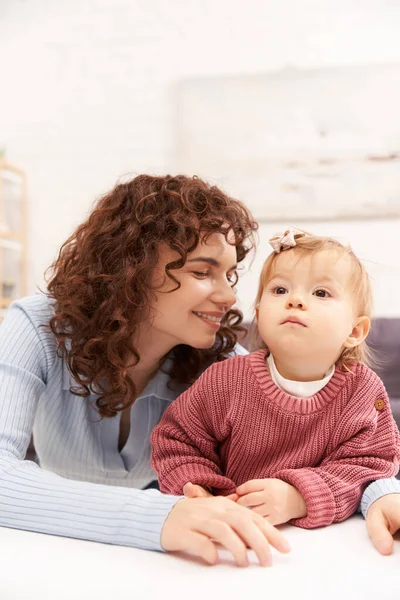 Portrait of cheerful woman and child, curly working mother hugging baby girl, balanced lifestyle, bonding, happy family time, modern parenting, engaging with kid, loving motherhood — Stock Photo