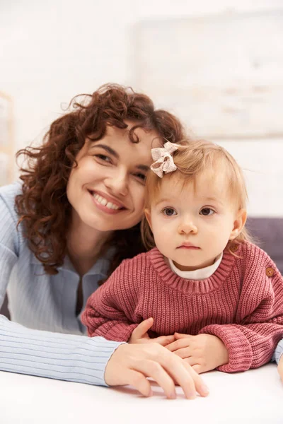 Portrait of cheerful woman and child, curly working mother hugging baby girl, balanced lifestyle, bonding, happy family time, modern parenting, joy, engaging with kid, loving motherhood — Stock Photo