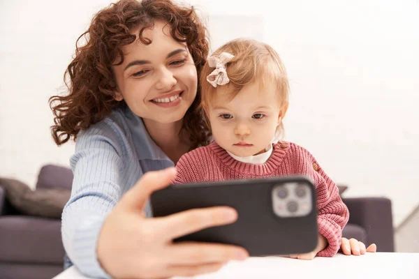 Selfie, parentalité moderne, femme gaie prenant selfie avec bébé fille, en utilisant un smartphone, enfant en bas âge et mère bouclée, portrait, ère numérique, relations familiales, engagement avec l'enfant, temps de qualité — Photo de stock