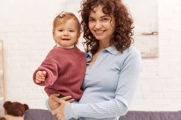Quality family time, working mother with curly hair holding in arms baby girl, woman and her toddler daughter, modern parenting, work life harmony, bonding and engaging with kid, happiness — Stock Photo