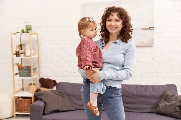 Balanced lifestyle, working mother with curly hair holding in arms baby girl, woman and her toddler daughter, modern parenting, work life harmony, bonding and engaging with kid, happiness — Stock Photo