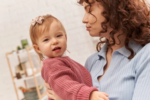 Balanced lifestyle, working mother with curly hair holding in arms baby girl, woman and her toddler daughter, work life harmony, bonding and engaging with kid, modern parenting — Stock Photo