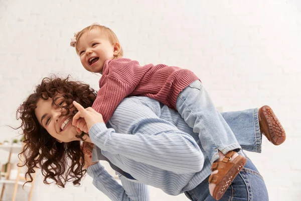 Quality time, happiness, balancing between work and life, cheerful woman with excited baby girl on back, mom daughter time, having fun together, bonding, loving motherhood, curly hair — Stock Photo